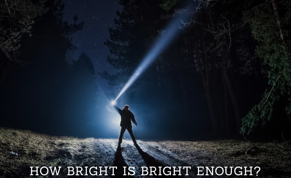 A person in dark woodland holding a torch above their head with a bright beam of light emitting from it, and text at the bottom that reads, 'how bright is bright enough?'